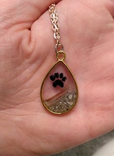 a person is holding a dog's paw in a tear shaped pendant