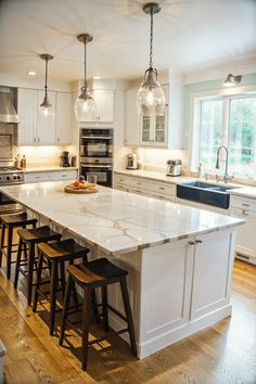 a large kitchen island with stools next to it and lights hanging from the ceiling