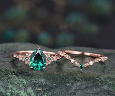 two rings with green and white stones on top of a mossy stone surface in front of a dark background