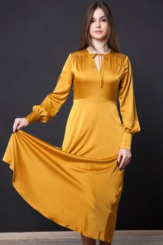 "Yellow dress featuring A-line silhouette, tea length, and a tear-drop neckline with ties. - tea length flowy skirt - long sleeves with cuffs - keyhole neckline with ties - draped bodice - concealed side seam zipper closure - patly lined (bodice and skirt) Color: Gold / Other Fiber: satin: viscose - 30%, elastane - 5%, polyester - 65 %. Lining: viscose - 30%, elastane - 5%, polyester - 65 %. For Size S (2 US): dress length - 48,5\" (123 cm) Our model wears size S (US 2) and is 165cm/5'4\" tall. Elegant Tea Length Maxi Dress For Wedding, Gold Midi Dress For Spring Wedding, Gold Midi Length Dress For Wedding, Elegant Tea-length Maxi Wedding Dress, Elegant Gold Midi Dress For Dinner, Elegant Gold Knee-length Midi Dress, Spring Wedding Gold Midi Dress, Silk Midi Tea Length Wedding Dress, Silk Midi Dress For Wedding In Tea Length