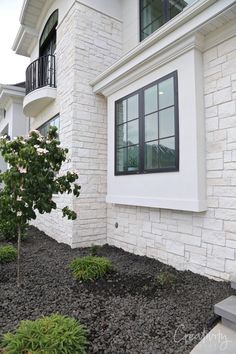 a white brick house with black windows and bushes in front of the window sill