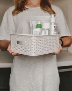 a woman holding a white basket filled with skin care products