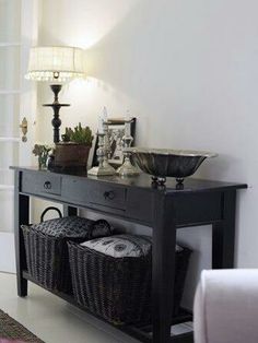 a black table with baskets underneath it and a lamp on the wall behind it in a living room