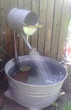 a metal bucket filled with water next to a wooden fence and a hose connected to it