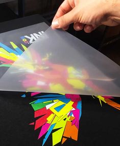 a person is cutting out some colorful art on a piece of clear paper with scissors