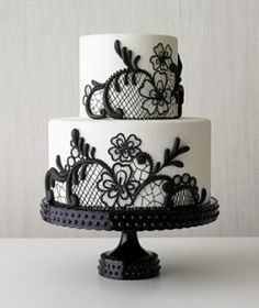 a three tiered cake with black lace and flowers on the top is decorated with white frosting