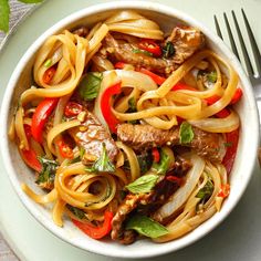 a white bowl filled with pasta and meat on top of a table next to a fork