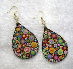 a pair of earrings with colorful designs on them sitting on a white surface in front of a towel