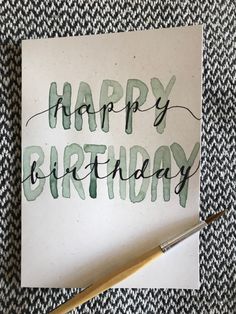 a card with the words happy birthday written on it next to a brush and paper