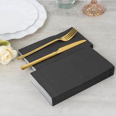 two forks and a knife are on top of a black book with a white rose next to it