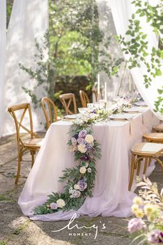 the table is set up with flowers and greenery for an outdoor wedding reception in front of white drapes