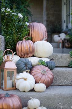 pumpkins and gourds sitting on the steps in front of a house with a lantern