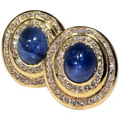 A pair of 14K yellow gold earrings centered around oval, cabochon, cut sapphires measuring 10mm X 12mm. Surrounding each sapphire, are two elliptical channels set with round brilliant cut diamonds. These modern earrings are set with a total of 2 sapphires weighing a total approximate weight of 14.25ct and 118 diamonds weighing a total of approximately 3.25ct. Signed Niva, they measure 1 inch long and 7/8 of an inch wide. Overall weight is 31.4 grams. Round Sapphire, Yellow Gold Earrings, Oval Earring, Yellow Gold Earring, Modern Earrings, Baguette Diamond, Emerald Diamond, Oval Cabochon, Oval Diamond