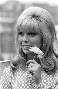 a black and white photo of a woman holding a flower in her hand while smiling