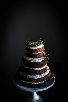 a three tiered cake with white frosting and sprigs on top sits on a plate