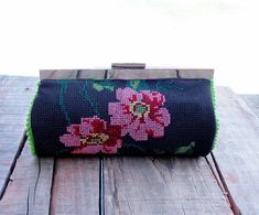 a black purse with pink flowers on it sitting on top of a wooden table next to a piece of wood