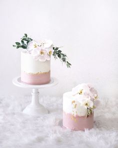 two cakes with white and pink frosting, one has flowers on the cake stand