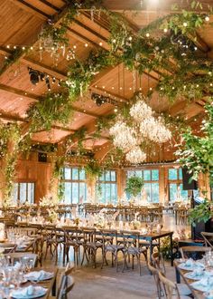 an indoor venue with tables and chairs covered in greenery, hanging chandeliers