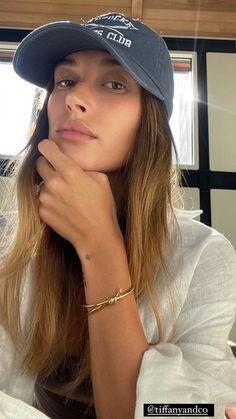 a woman with long hair wearing a hat and looking off to the side while sitting in front of a window