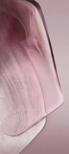 a pink and white glass vase sitting on top of a wooden table next to a wall