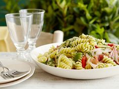 a white bowl filled with pasta salad next to two empty wine glasses on a table