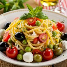 a pasta salad with tomatoes, olives and mozzarella on a white plate