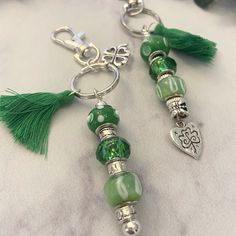 two green glass beads with tassels are hanging from key chains on a white surface