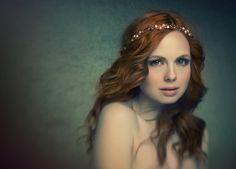 a woman with long red hair wearing a headband and looking at the camera while standing in front of a dark background