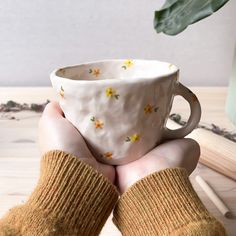 a person holding a coffee cup in their hands on a wooden table next to a potted plant