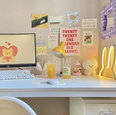 a white desk topped with a computer monitor next to a yellow lamp and other items