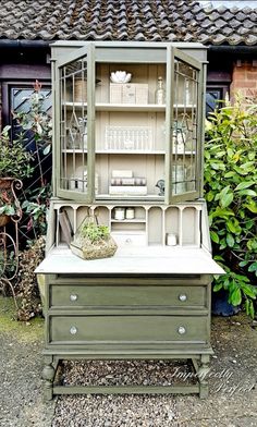 an old dresser with glass doors and drawers in front of some plants on the ground