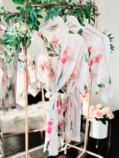 a floral robe hanging on a rack in front of a mirror with flowers and greenery