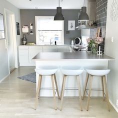 three white stools sit at the center of a kitchen island in front of a window