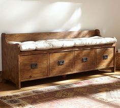 a wooden bench sitting on top of a floor next to a rug and window sill