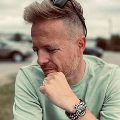 a man with a watch on his wrist sitting in front of a parking lot and looking at the camera