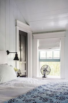 a bedroom with a bed, window and fan on the wall next to the window