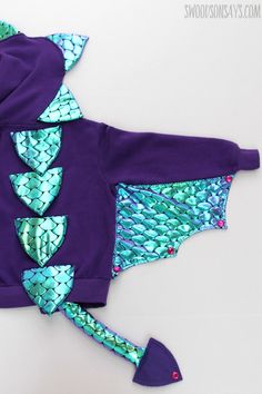 a purple jacket with green and blue sequins is laying on top of a white surface