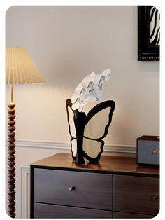 a black vase with white flowers in it on top of a dresser next to a lamp