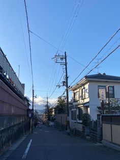 an empty street with power lines above it and houses on the other side in the distance