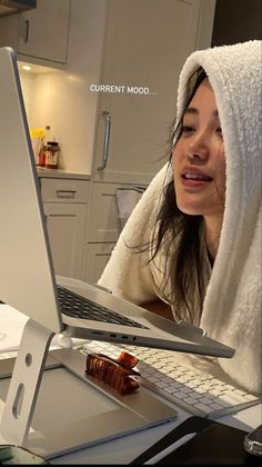 a woman with a towel on her head is looking at a laptop screen and smiling