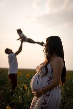 a pregnant woman standing in a sunflower field with her husband holding the baby's hand