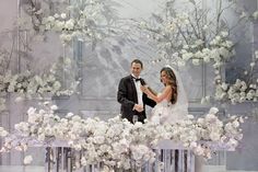 a bride and groom standing in front of a floral display at a wedding ceremony with white flowers