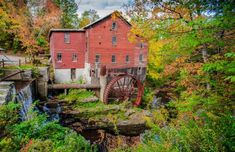 an old mill in the woods with fall foliage around it and a water wheel on the side