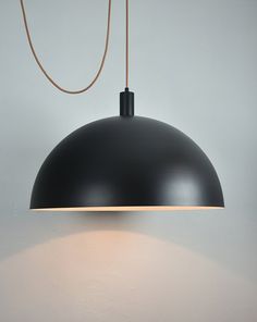 a black lamp hanging from the ceiling with a white wall behind it and a brown cord