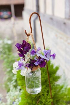 purple and white flowers in a mason jar hanging from a tree branch with an umbrella