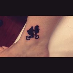 a small tattoo on the ankle of a person riding a bike with a baby in it