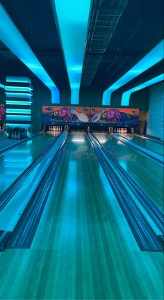 a bowling alley filled with blue bowling lanes and neon lights on either side of the lanes