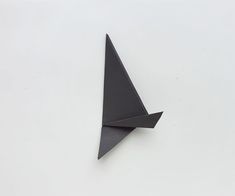 a black origami bird on a white surface with one wing folded in the shape of a triangle