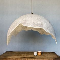 a white lamp hanging from the ceiling over a wooden table with a cup on it