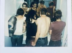 a group of people standing around each other in front of a bathroom mirror with their backs turned to the camera